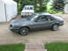 1985 Ford Mustang - A gray 1985 Ford Mustang is parked on a gravel driveway next to an SUV and a white tent.