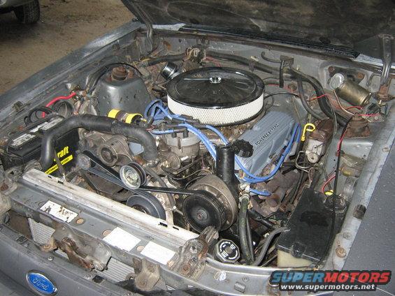 Engine bay of a Ford vehicle, showing V8 engine, air filter, battery, and radiator