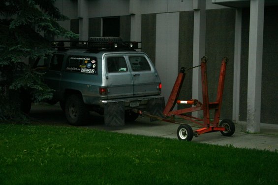 Blue SUV with roof rack and spare tire, towing a red trailer