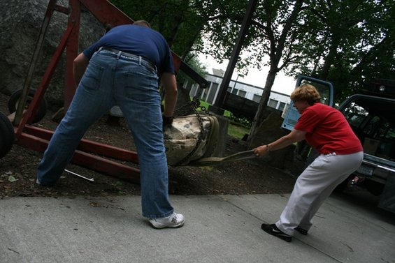 Blue pickup truck with open door, people moving a rock with a crane