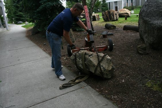 Man using trolley jack to move large rock on straps