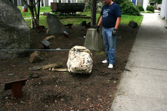 Rock garden scene with a man standing next to a large, tarp-covered rock