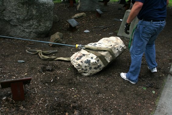 Rock being pulled by a strap and cable, with a person in jeans and sneakers guiding it