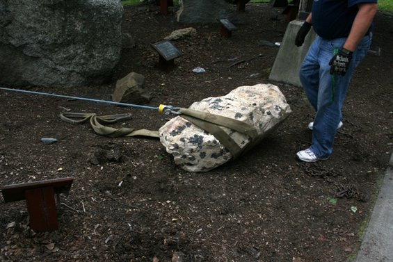 Person in jeans and gloves pulls a rock with a strap and cable