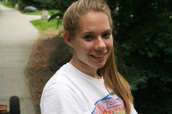 Young woman with blonde hair in a ponytail, smiling at the camera, wearing a white t-shirt