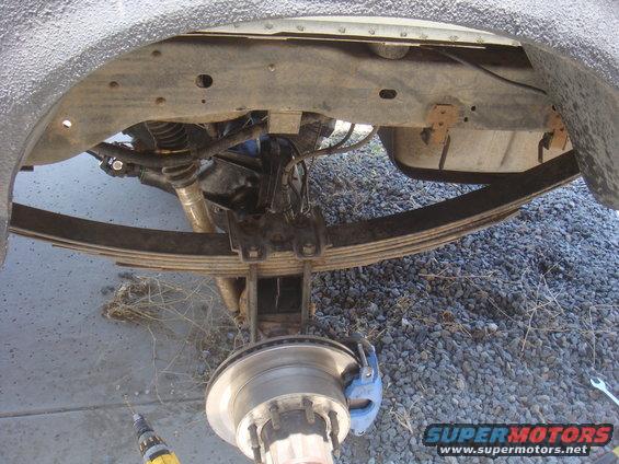 Rear axle assembly with leaf springs, brake caliper, and hub. Textured fender liner above
