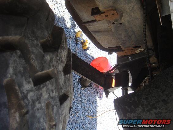 Undercarriage view of a vehicle's suspension and large tire. Supermotors.net logo visible