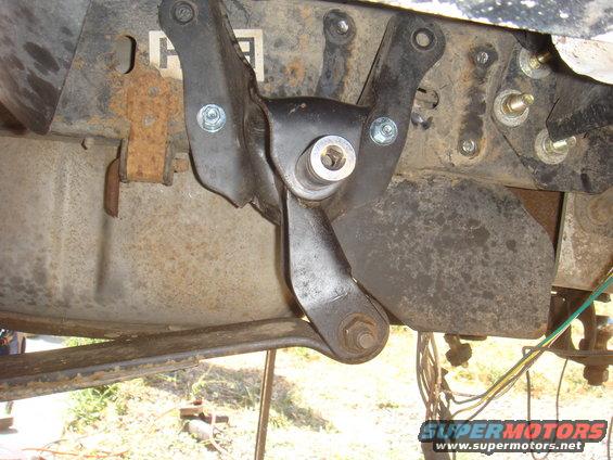 Close-up of a black metal suspension component attached to a rusty frame with bolts and a nut