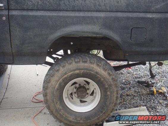 Side view of a lifted Ford Bronco's rear wheel well and tire. Tools are on the ground nearby