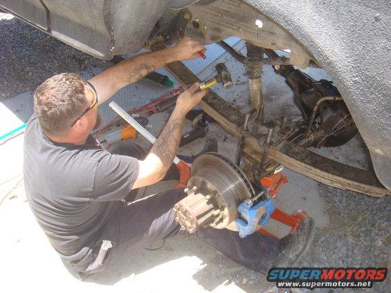 Man with hammer working on vehicle's rear axle and suspension components