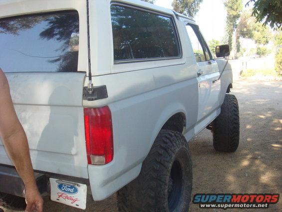 White 1992 Ford Bronco with lifted suspension and large off-road tires, rear quarter view. License plate reads 'Ford Racing'