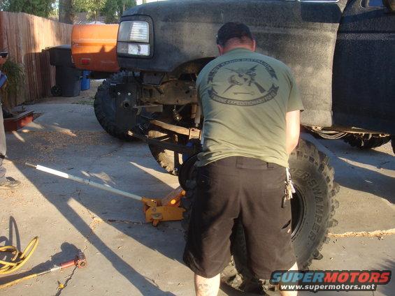 Black truck front end being serviced with a jack; orange truck in background