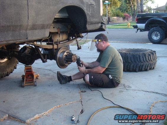 Man grinding on rear axle of vehicle, another truck in background