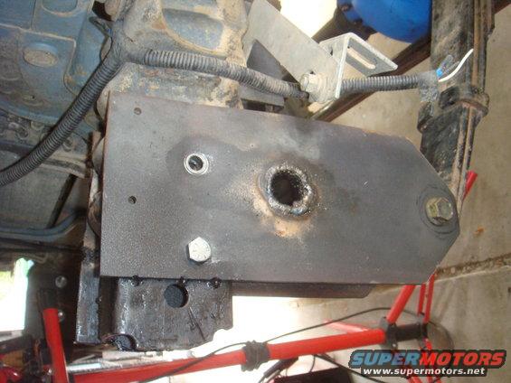 Close-up of a metal bracket bolted to a vehicle's frame, showing a hole with rough edges