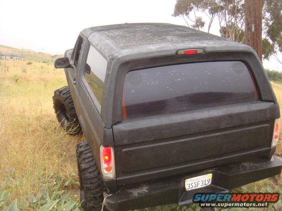 Black SUV with large off-road tires parked in a grassy field. Rear view shows tinted windows and a California license plate