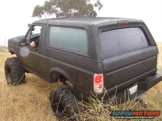 Black 1992 Ford Bronco with lifted suspension and oversized tires parked in dry grass