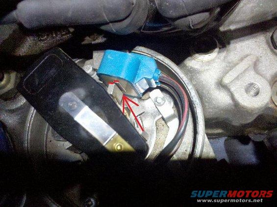 Close-up of a vehicle's ignition distributor cap and rotor with a red arrow pointing to the rotor tip