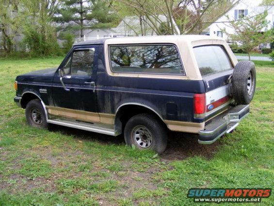 Dark blue and tan Ford Bronco parked on grass. Spare tire mounted on rear