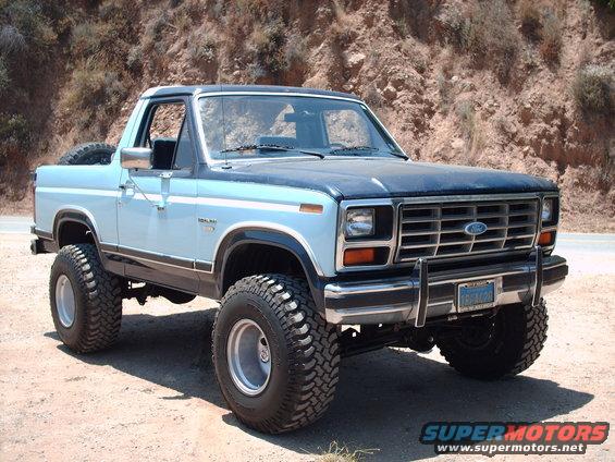 Lifted blue and black Ford Bronco parked on dirt road with rocky hillside behind