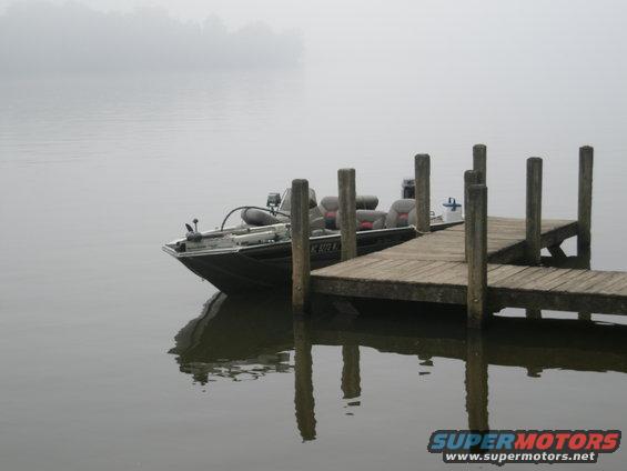 Bass boat docked on a foggy lake, with wooden posts and reflections