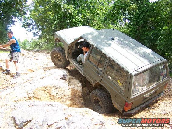 Olive green Jeep Cherokee XJ with lifted suspension navigating rocky terrain