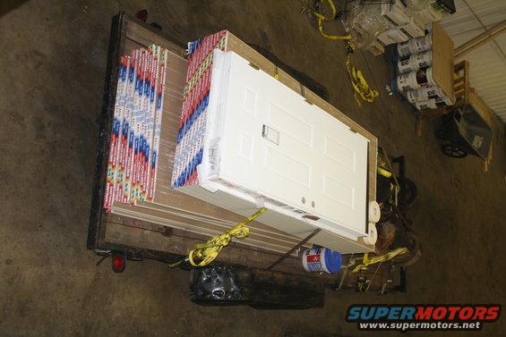 trailer loaded with doors and stacks of drywall, secured with yellow straps
