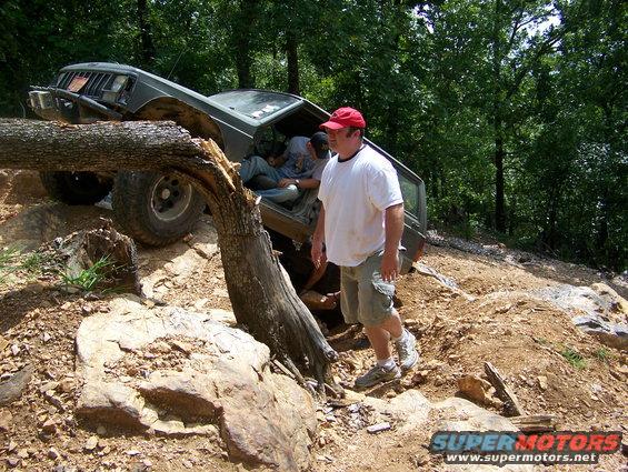 Jeep Cherokee XJ navigating a rocky, wooded trail with a fallen tree blocking the path