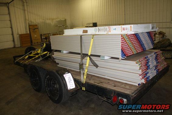 Trailer loaded with stacks of drywall sheets, secured with yellow straps. License plate reads 227506
