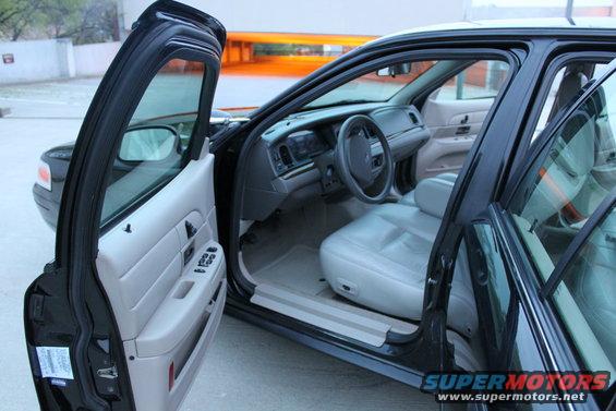 Interior of a black Ford Crown Victoria with light-colored seats and dashboard. Front doors are open