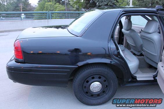 Black 2007 Ford Crown Victoria sedan, rear quarter view, open doors showing grey interior, steel wheels