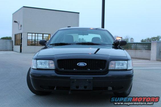 Black Ford Crown Victoria front view, parked on a concrete surface, with a building in the background