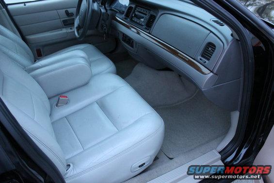 Interior of a car with light gray leather seats and a wood-grain trim dashboard. The steering wheel and center console are visible