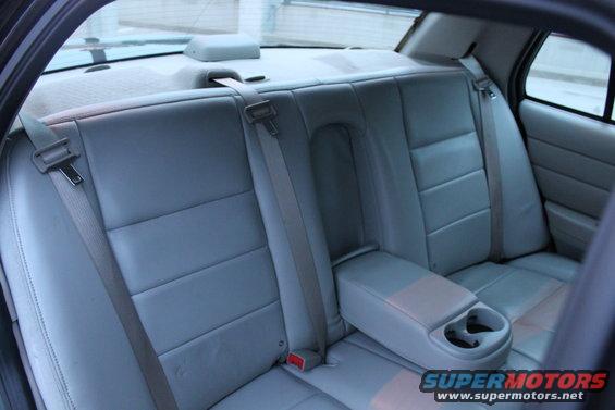 Gray leather rear car seats with seatbelts and a center console armrest with cup holders