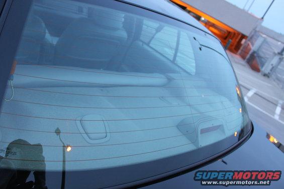 Rear window of a dark-colored car with defroster lines and interior reflection