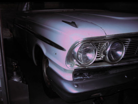 Front corner of a light-colored 1960s Ford Fairlane. Dual headlights and grille visible