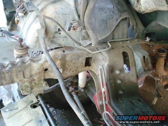 Rusty vehicle frame with engine parts, hoses, and a shock absorber visible