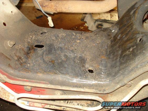 Close-up of rusty vehicle frame with exhaust pipe above. Some wires are visible