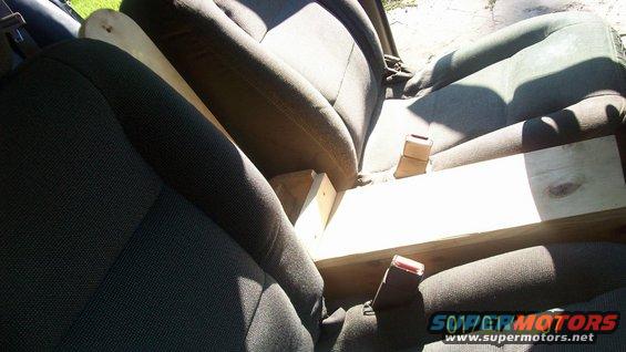 Car interior showing front seats with a wooden plank placed between them