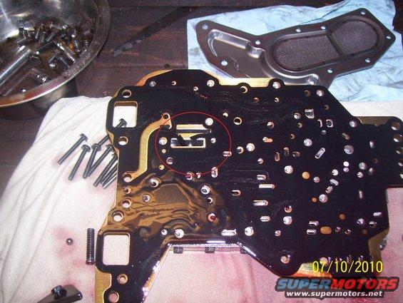 Automatic transmission valve body with a red circle highlighting a component, parts and tools nearby