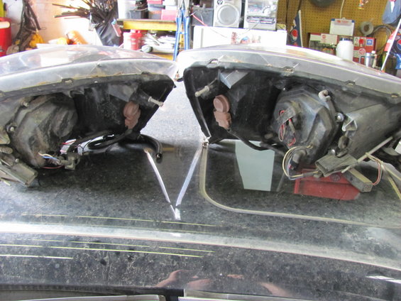Two disassembled vehicle headlights with exposed wiring and bulb sockets, resting on a dark surface