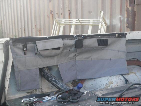 Tailgate organizer with multiple pockets and straps, mounted inside a vehicle bed