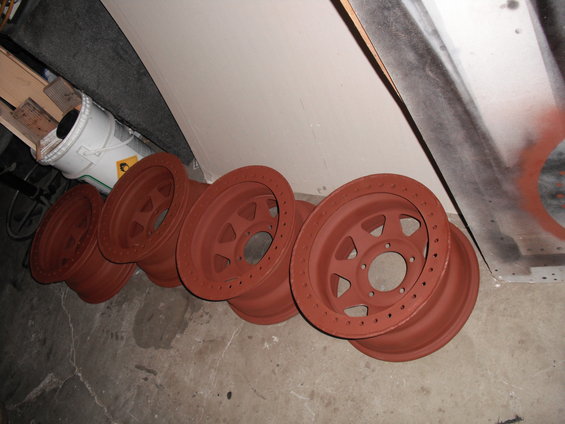 Five red primer painted wheels lined up on a concrete floor