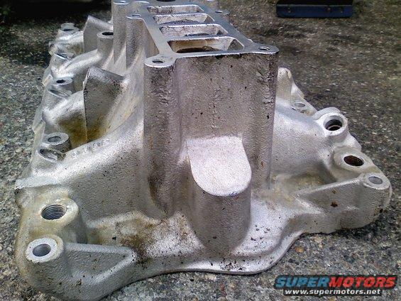 Aluminum intake manifold with multiple ports and bolt holes, resting on a concrete surface