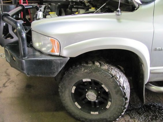 Silver pickup truck front fender and wheel with aftermarket bumper
