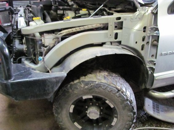 Front fender and wheel of a silver truck with exposed engine components