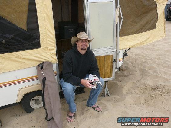 Man in cowboy hat sits in open pop-up camper on sandy beach