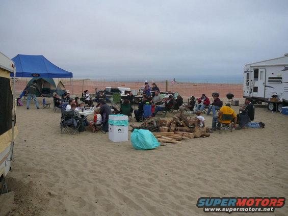 Beach gathering with RVs, tents, and people sitting around a fire pit