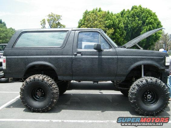 Lifted black SUV with large tires, hood open, parked outside