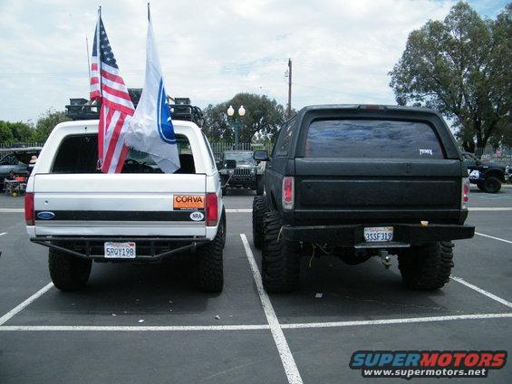 Rear view of a white and a black lifted Ford Bronco, both with aftermarket bumpers