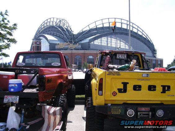 Rear view of red Ford and yellow Jeep pickup trucks, Miller Park in background
